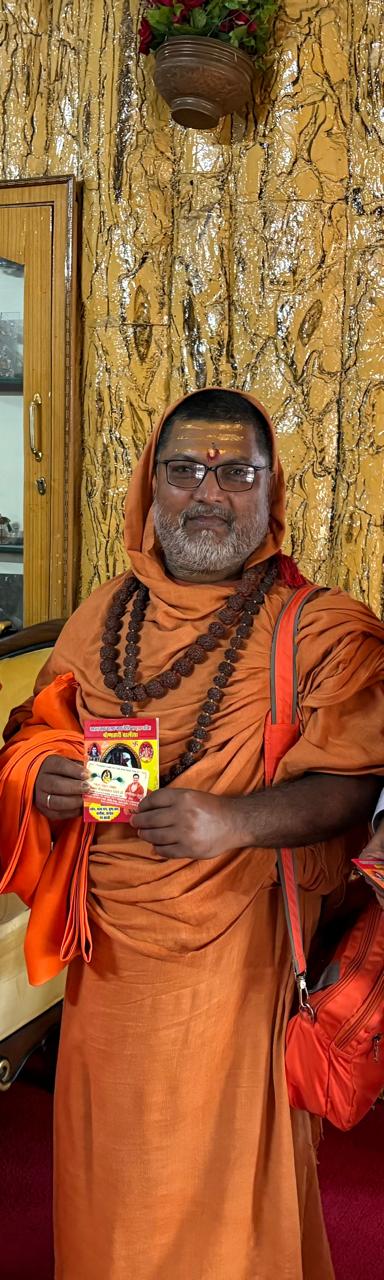 Guruji holding the Ashram's Panchang almanac — आश्रम का पंचांग हाथ में लिए हुए गुरुजी